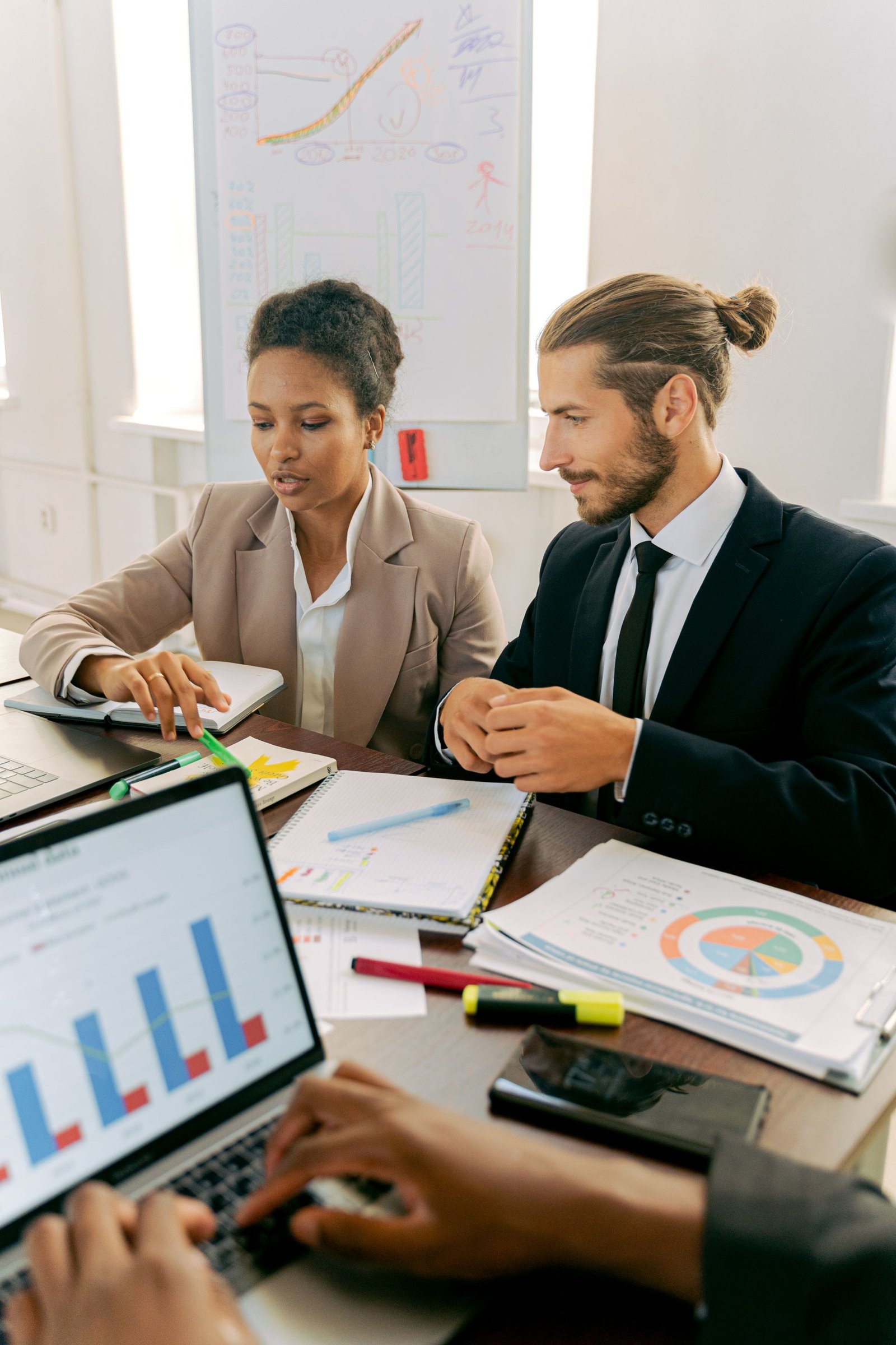 Two business colleagues in suits reviewing charts together at an office desk