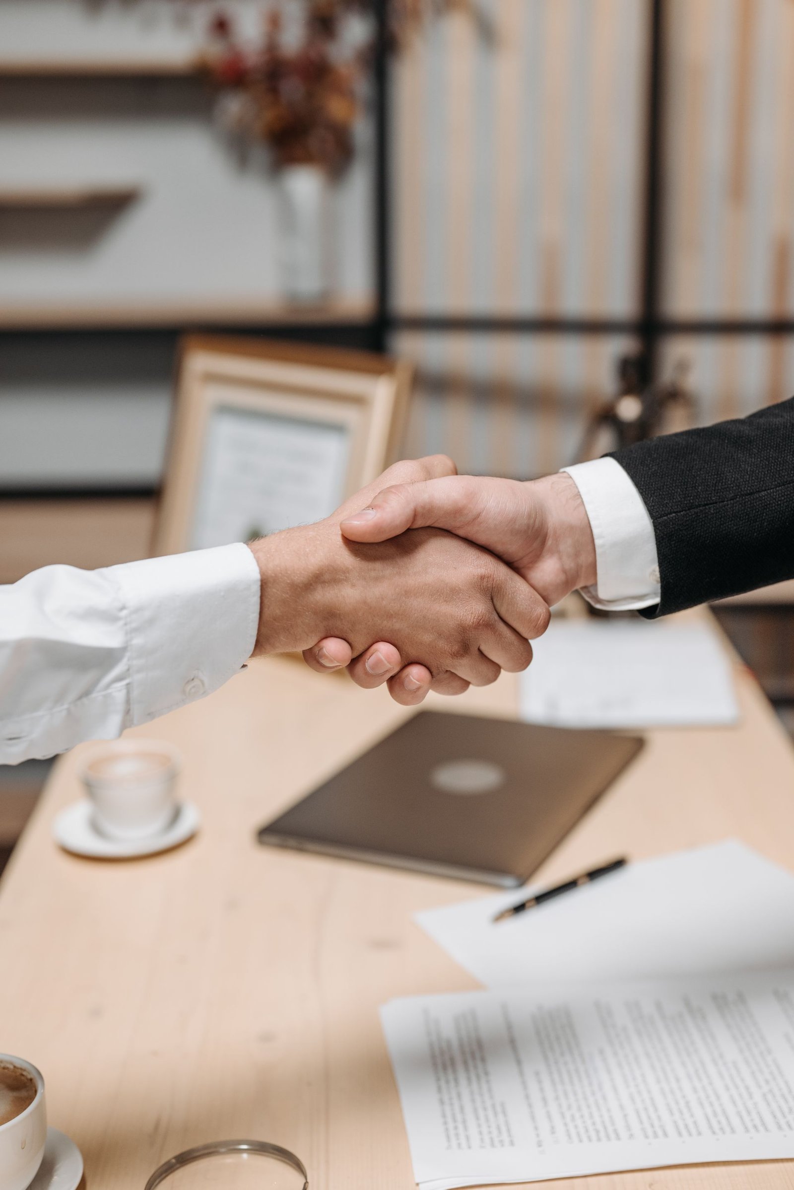 Two people shaking hands across a desk after a meeting