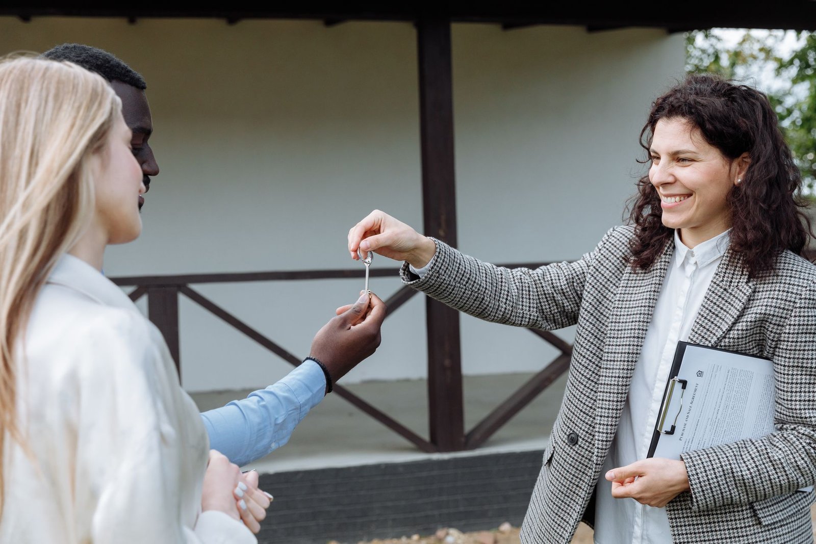 A smiling agent handing the keys of a new home to its new residents outside the house
