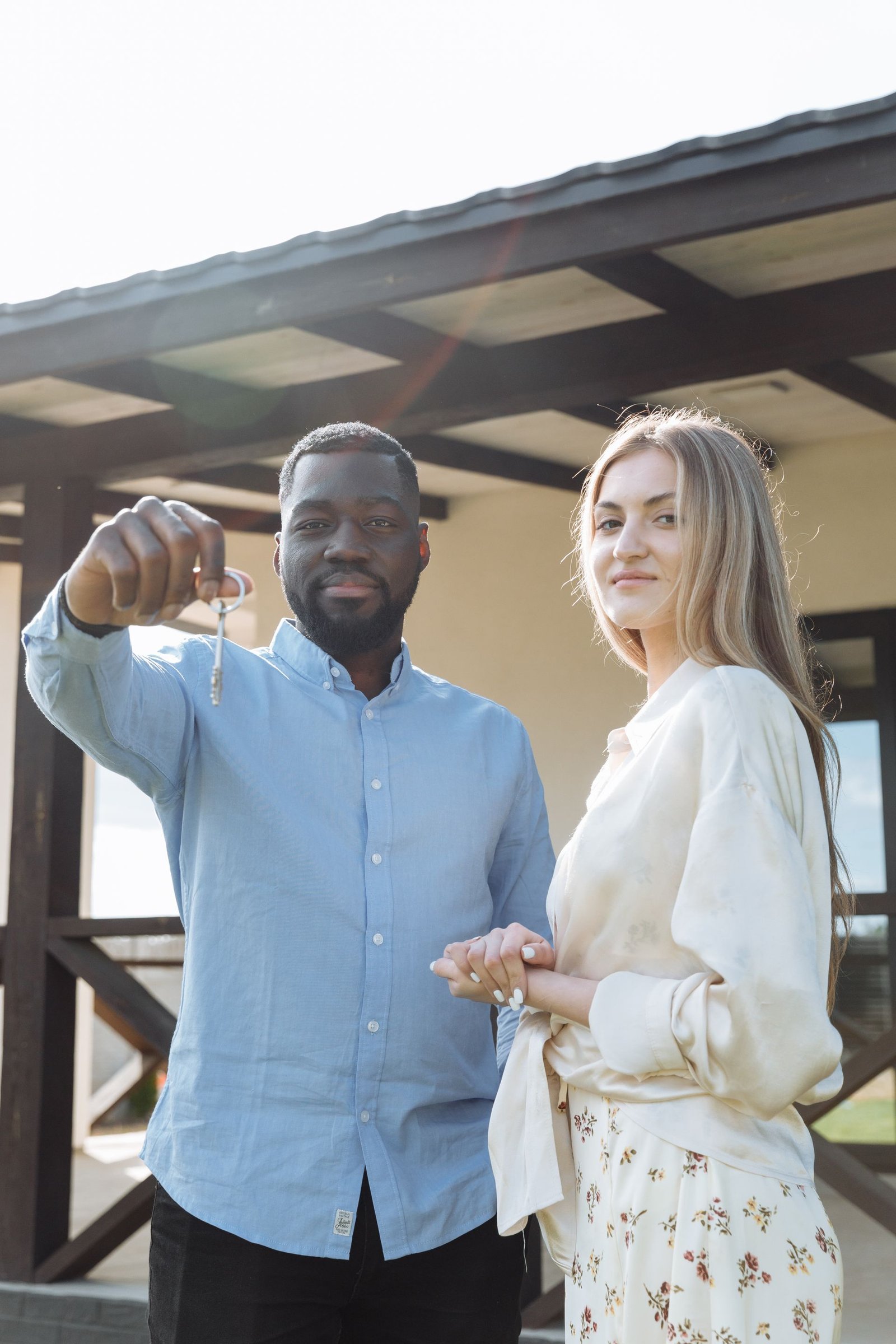 A smiling couple holding up the keys to their new home on the front porch