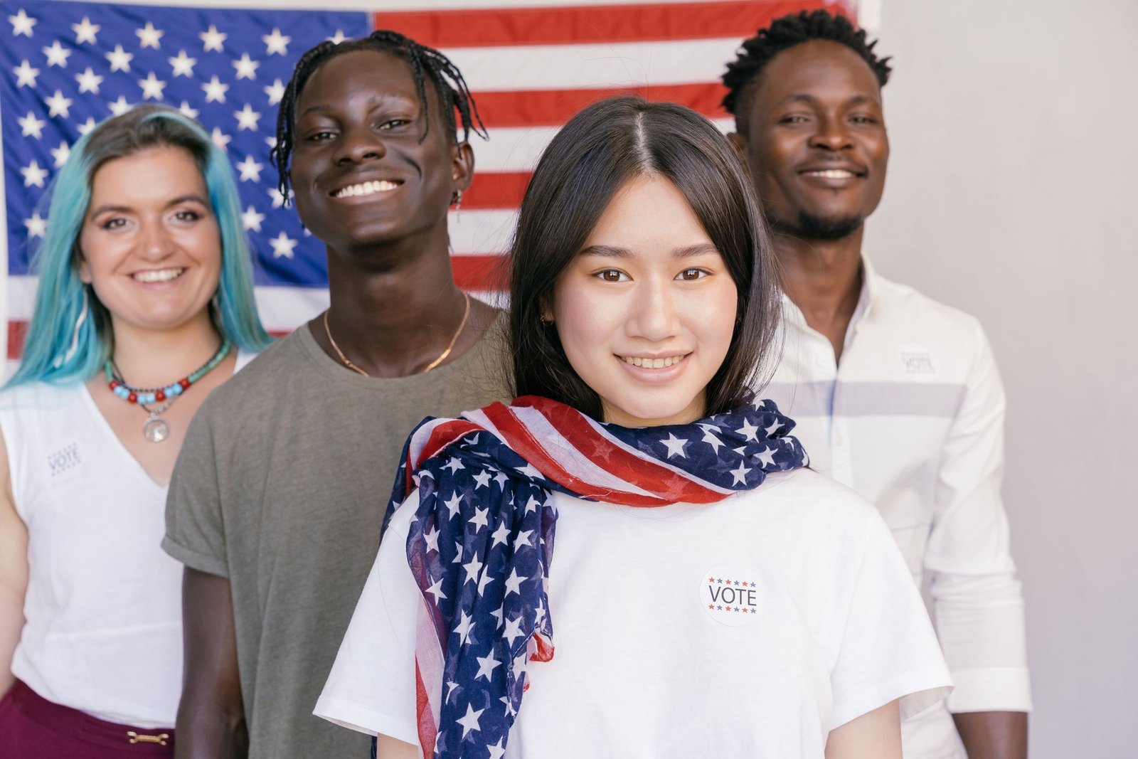 A smiling group of young people standing in front of an American flag