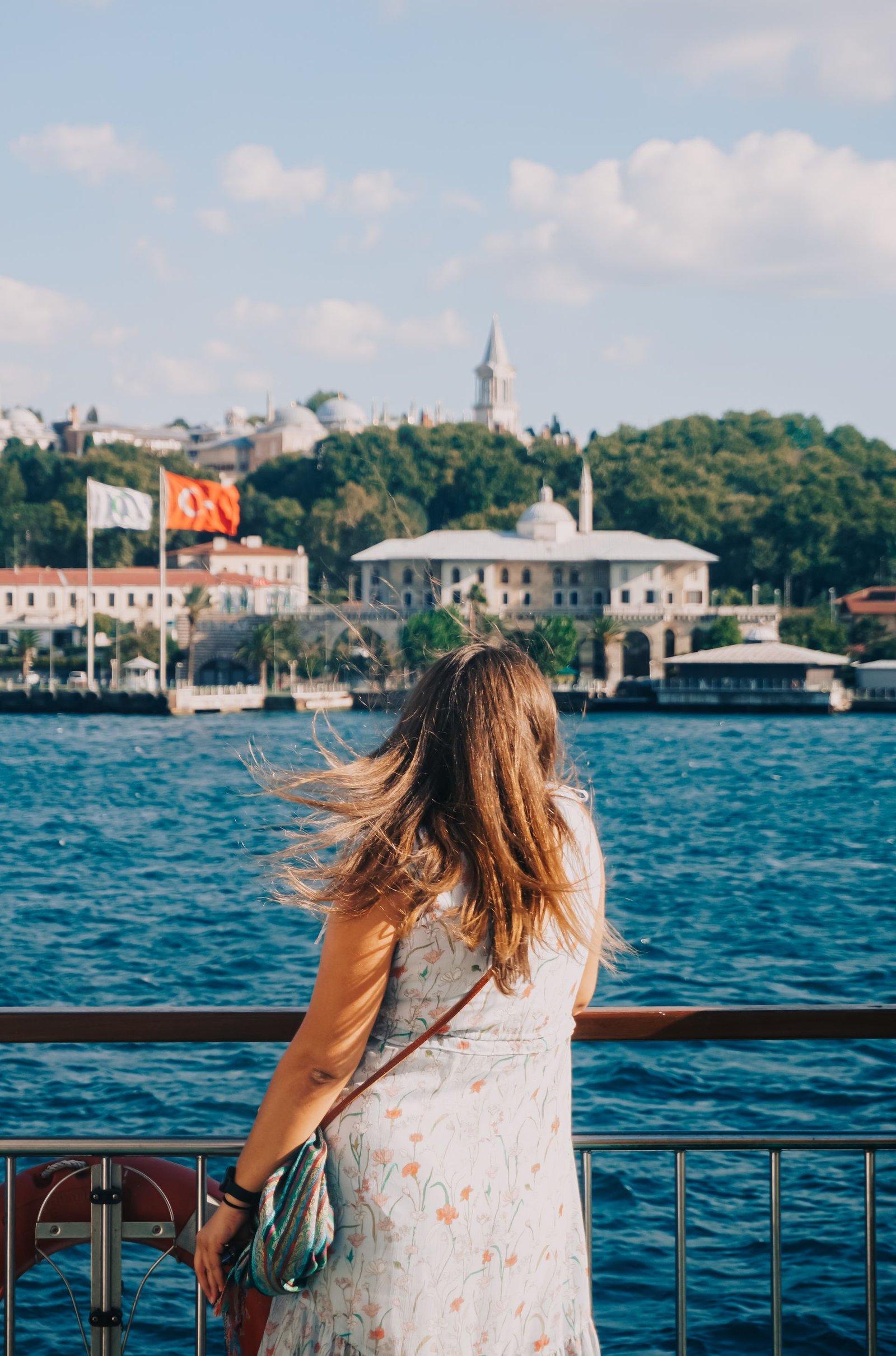 A traveler leaning on a ferry railing, looking across the water at a historic waterfront